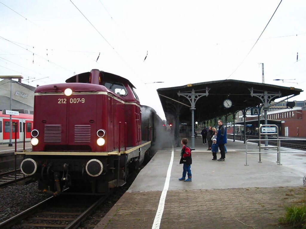 Locomotive diesel rouge DB 212 007-9 sur les rails en gare.