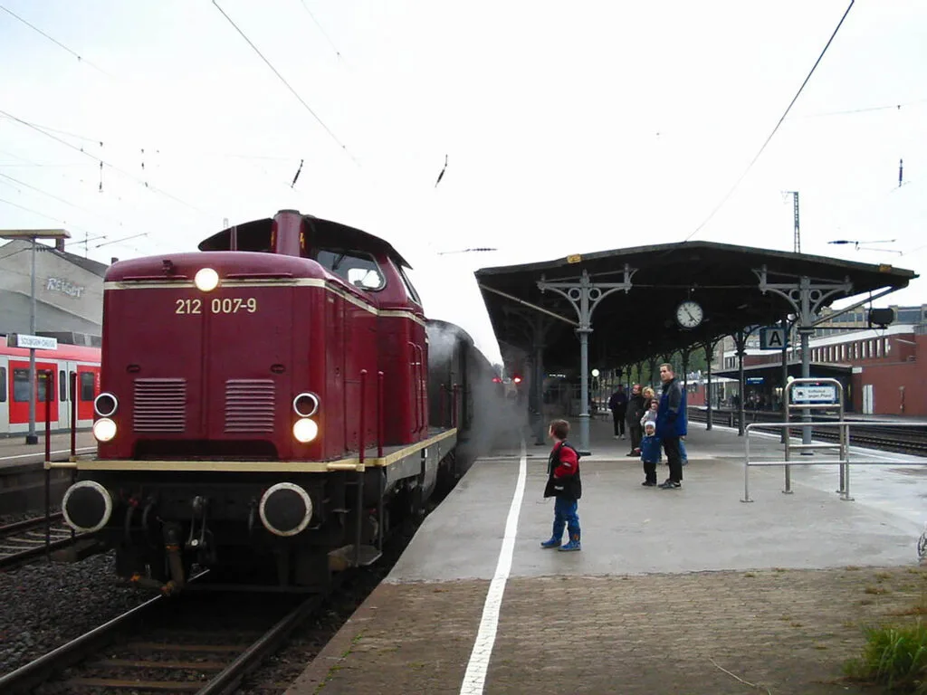 Locomotive diesel rouge DB 212 007-9 sur les rails en gare.