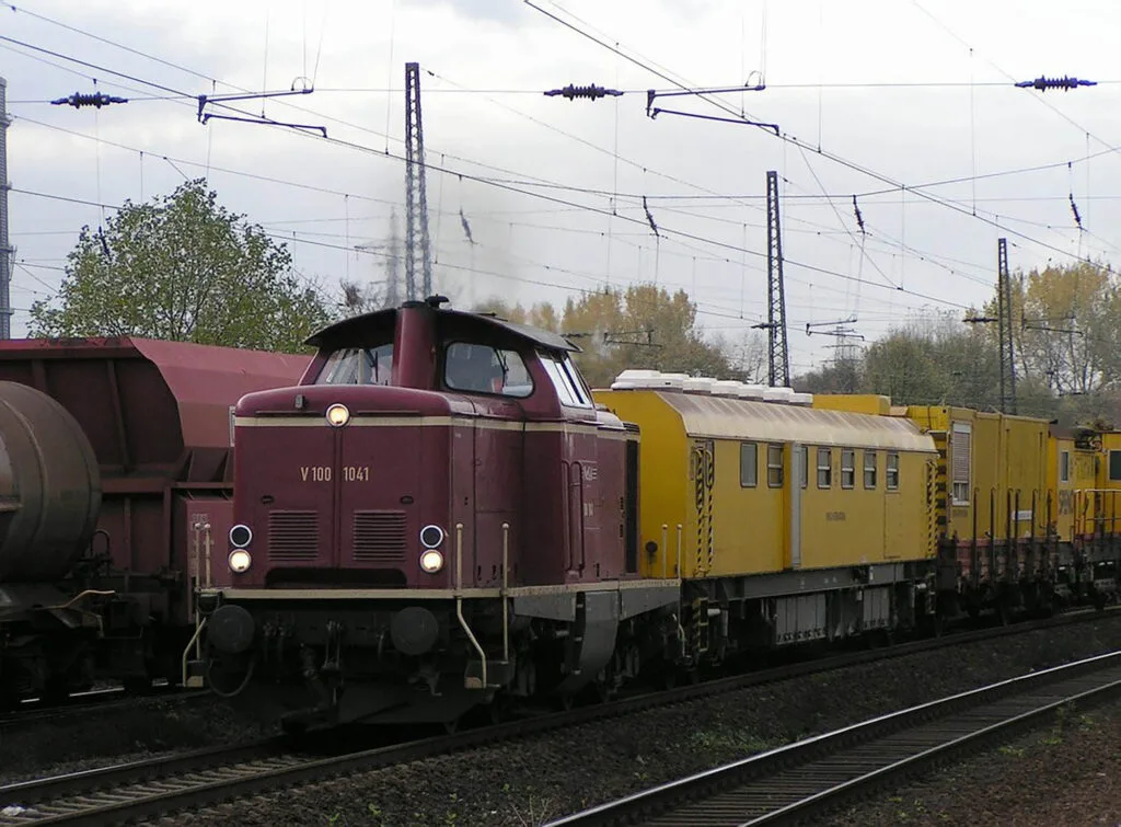 Locomotive V100 de l'entreprise NeSA, bordeaux et wagon jaune sur rails électrifiés