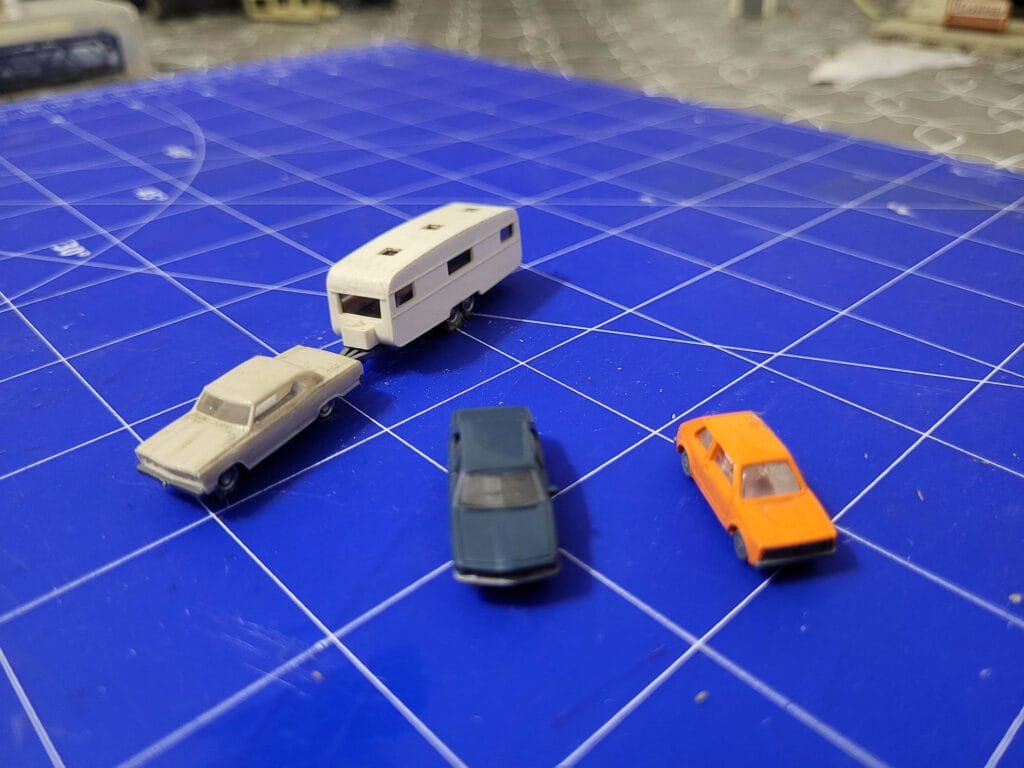 Miniatures voitures et caravane sur plateau bleu quadrillé