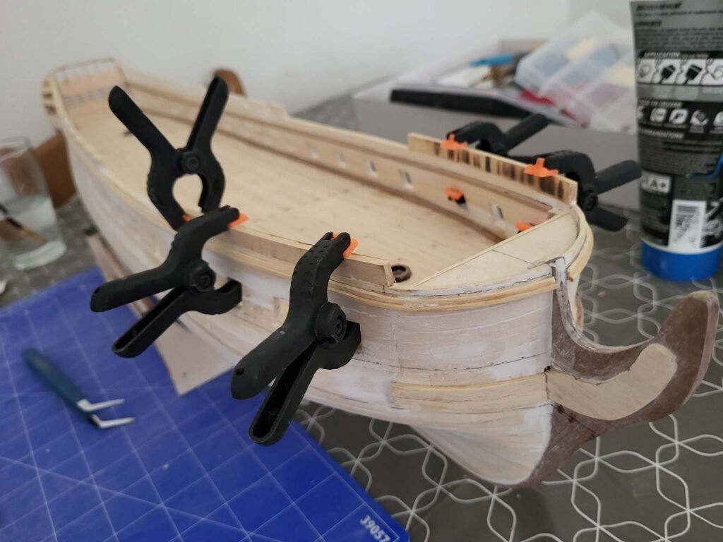 Maquette de bateau en bois avec serre-joints noirs et orange maintenant assemblage bois menuiserie