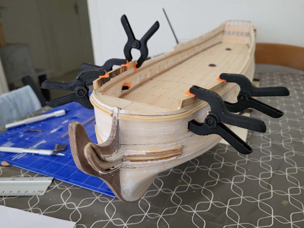Maquette de bateau en bois avec serre-joints noirs et orange maintenant assemblage bois menuiserie