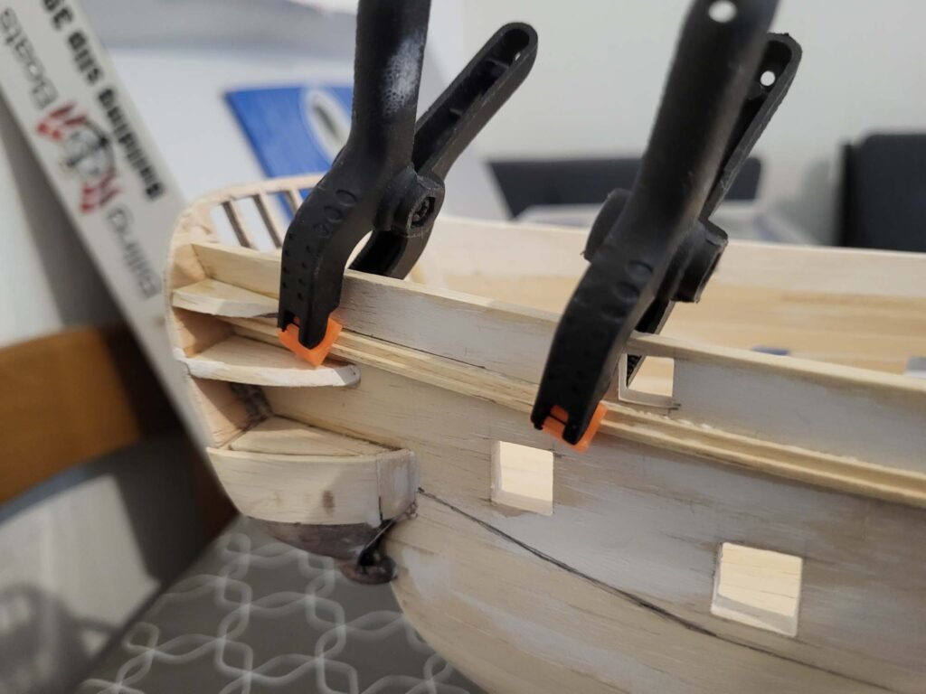 Maquette de bateau en bois avec serre-joints noirs et orange maintenant assemblage bois menuiserie
