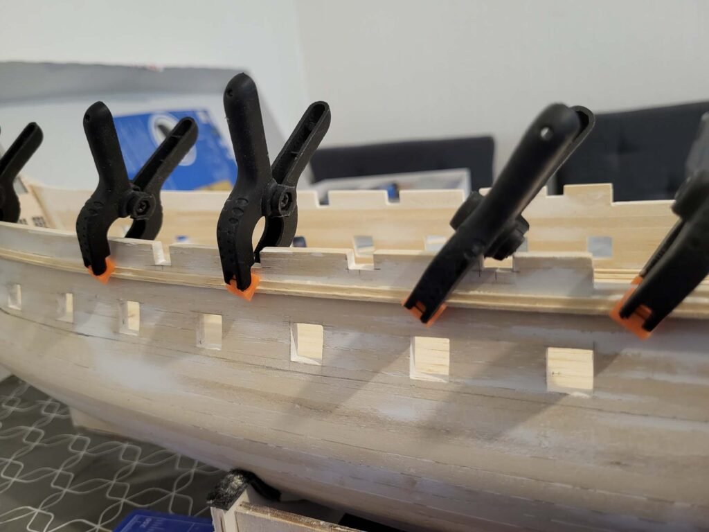 Maquette de bateau en bois avec serre-joints noirs et orange maintenant assemblage bois menuiserie
