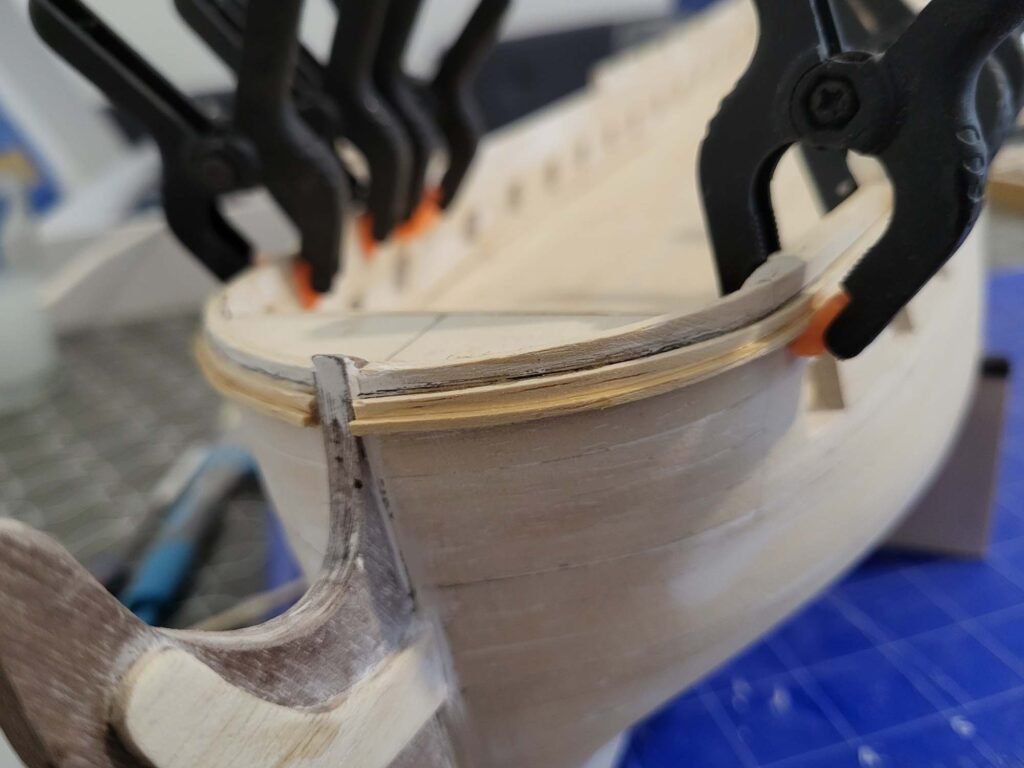 Maquette de bateau en bois avec serre-joints noirs et orange maintenant assemblage bois menuiserie